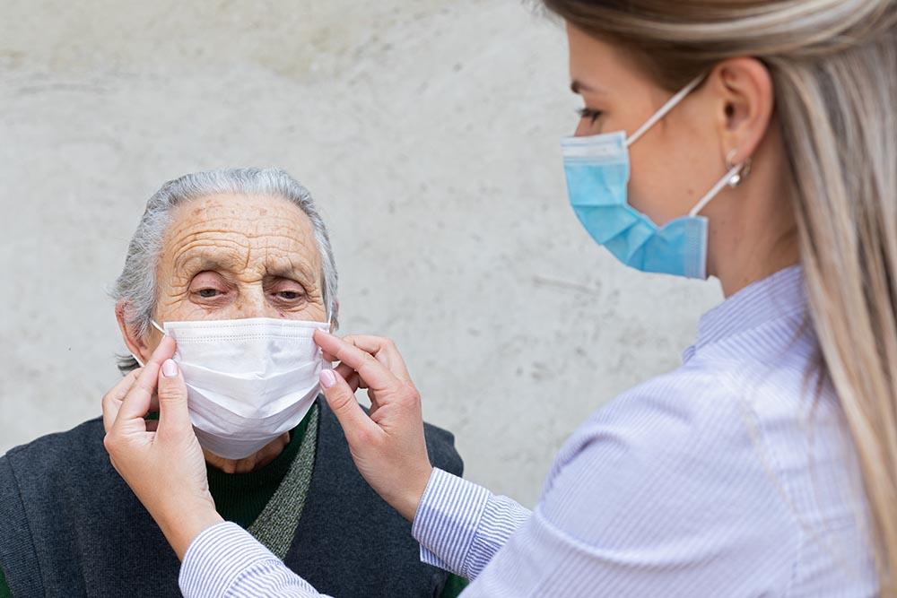 A lady putting a mask on an elderly woman with Alzheimer's disease before their estate planning checkup