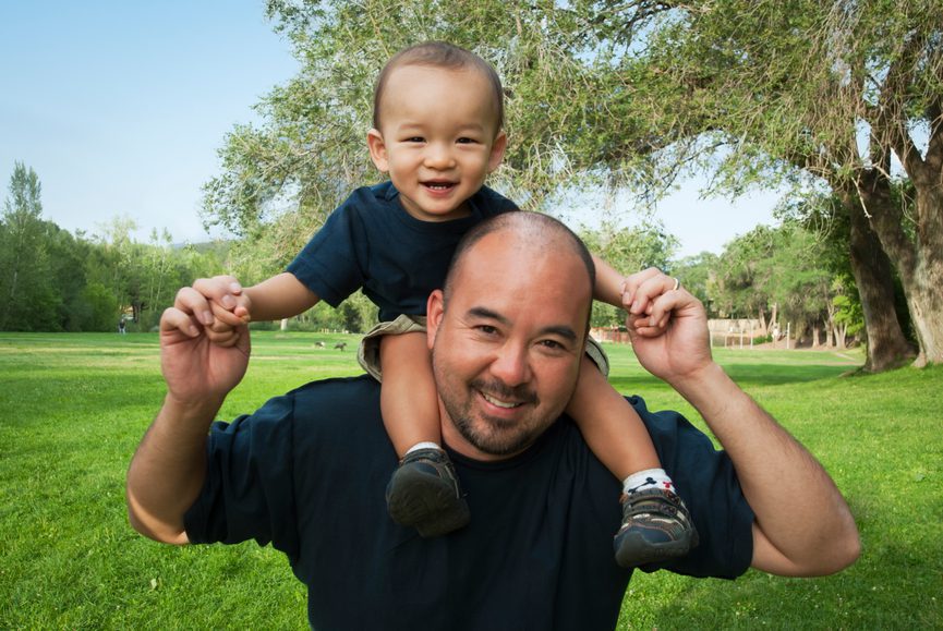 A 18-month-old baby boy and his father (Caucasian - Japanese mix), riding piggyback at a park.